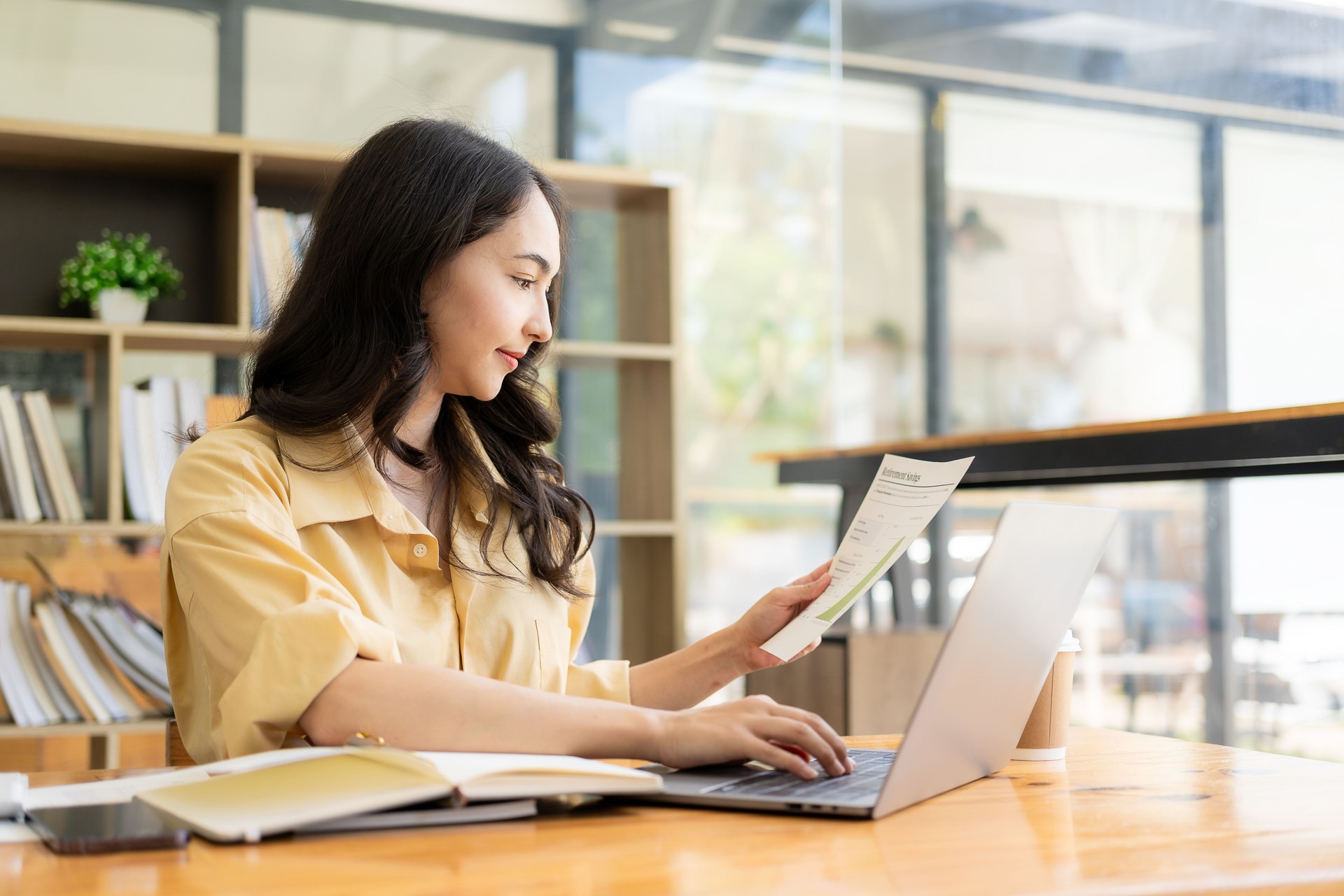 Ambitious Asian girl working from home Looking at laptop screen and financial documents, woman is checking email or doing research while working remotely.